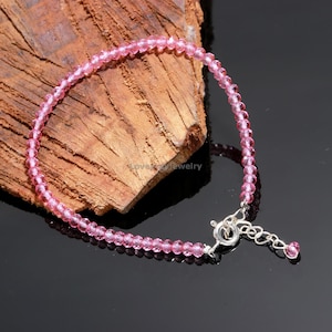May include: A pink crystal bead bracelet with a silver clasp and a small pink crystal charm.