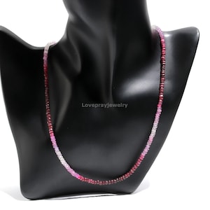 May include: A pink and red gemstone necklace with graduated beads. The necklace is made of faceted, square-shaped beads that are strung on a silver chain.