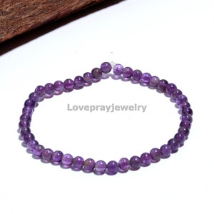 Könnte beinhalten: Ein violettes Amethyst-Perlenarmband mit einem silbernen Verschluss. Das Armband besteht aus kleinen, runden Perlen und ist etwa 18 cm lang.