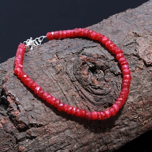 May include: A red gemstone beaded bracelet with a silver clasp. The bracelet is on a wooden surface.