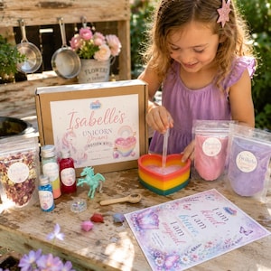 May include: A unicorn potion kit featuring a cardboard box labelled Isabelle's Unicorn Dreams Potion Kit, a heart-shaped rainbow bowl, a wooden spoon, a dropper, small bottles of coloured liquids, pouches of powders, and a printed affirmation card.