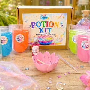 May include: A potion kit set featuring a cardboard box labelled Potion Kit, a pink lotus-shaped bowl, a small bottle of sparkle syrup, a clear dropper, and several pouches of colourful Magic Fizz Dust in yellow, blue, orange, green, pink, and purple.