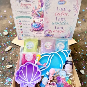 May include: A craft kit box featuring a Mermaid Lagoon instruction card and a sign stating I am calm, I am wonder, I am magic. Contents include a purple shell bowl, a blue shell tray, a mermaid figurine, coloured powders, crystals, and bottles.