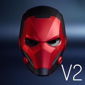 Op de afbeelding: Een rood en zwarte helm met een futuristisch ontwerp. De helm heeft een prominente vizier en een gesegmenteerd frontpaneel. De tekst "V2" wordt in het wit weergegeven. De algehele esthetiek suggereert een superhelden- of sci-fi-thema.