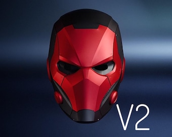 Può includere: Un casco rosso e nero dal design futuristico. Il casco presenta una visiera prominente e una placca frontale segmentata. Il testo "V2" è visualizzato in bianco in basso. L'estetica generale suggerisce un tema supereroistico o fantascientifico.