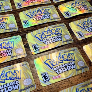 May include: Multiple rectangular cards with the "Pokémon Recharged Yellow" logo in blue and yellow. The cards have a yellow background with a holographic effect. The cards also feature the Nintendo logo and an "E" rating.