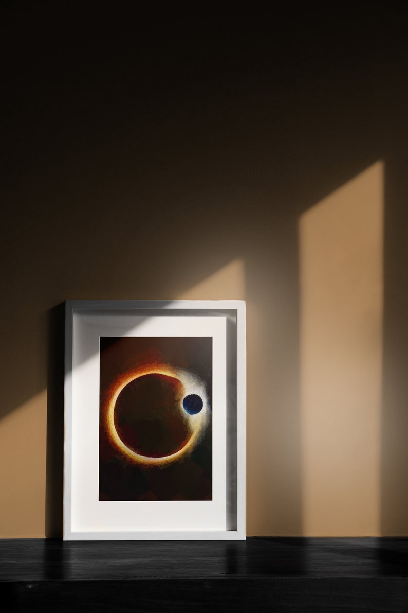 May include: A framed print of a dark, abstract painting depicting a ring of light around a small, blue circle. The painting is in a white frame and is hanging on a wall.
