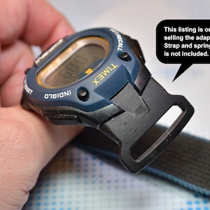 May include: A blue and black Timex watch with a black strap adapter. The watch face has a yellow border and the words "INDIGLO" and "RECALL" are printed on the watch face. The text "This listing is only selling the adapter. Strap and spring bar is not included." is in a speech bubble.
