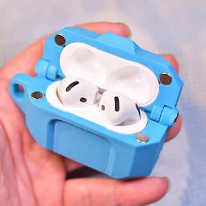 May include: A light blue protective case for wireless earbuds, open to reveal two white earbuds. The case has a geometric design with silver and bronze accents. The earbuds are white with black details.