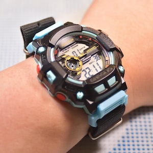 May include: A black and blue digital wristwatch with a black band. The watch face has a multi-layered design with a large digital display and smaller analog displays. The watch has a blue and black strap.