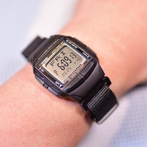 Puede incluir: Reloj de pulsera digital negro con una correa de nailon negra. La esfera del reloj muestra la fecha, la hora y el día de la semana. La esfera del reloj muestra "FRI 1 6:09 20 23".