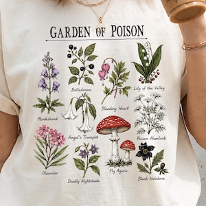 以下が含まれることがあります： GARDEN OF POISONというタイトルの植物イラストが描かれたクリーム色のTシャツ。グラフィックには、Monkshood、Belladonna、Bleeding Heart、Lily of the Valley、Angel's Trumpet、Poison Hemlock、Oleander、Deadly Nightshade、Fly Agaric、Black Helleboreといったラベルが付いた様々な植物やキノコが描かれています。