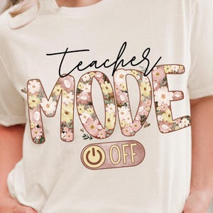 May include: A white t-shirt with the text "teacher mode off" in pink and brown lettering. The word "mode" is decorated with pink and yellow floral designs. A pink and gold power button with the word "off" is below the text.
