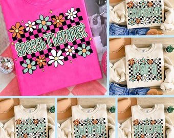 May include: A collection of t-shirts and sweatshirts with profession-themed designs. The bright pink t-shirt features the words "Speech Therapist" with a checkerboard pattern and flower accents. Other sweatshirts say "Counselor", "Para", "Teacher", "Librarian", and "Principal".