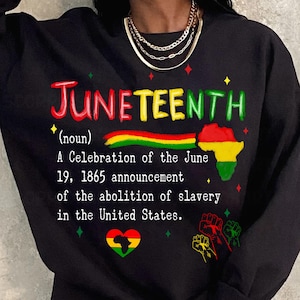 Może przedstawiać: Czarna bluza z napisem "JUNETEENTH" w kolorze czerwonym, żółtym i zielonym. Projekt zawiera kolorowy kontur kontynentu afrykańskiego i tekst wyjaśniający znaczenie święta, upamiętniający zniesienie niewolnictwa w Stanach Zjednoczonych.