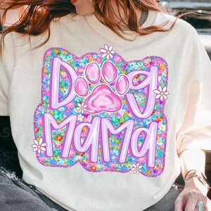 May include: A white sweatshirt with a purple and pink paw print and the text "Dog Mama" surrounded by colorful flowers.