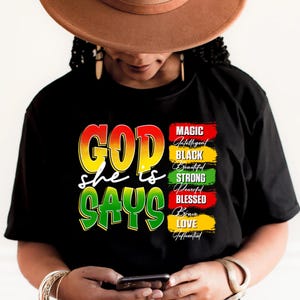 May include: Black t-shirt with the words "GOD she is SAYS" in yellow, red, and green. The shirt also features a list of words: Magic, Intelligent, Black, Beautiful, Strong, Powerful, Blessed, Brave, Love, and Influential.