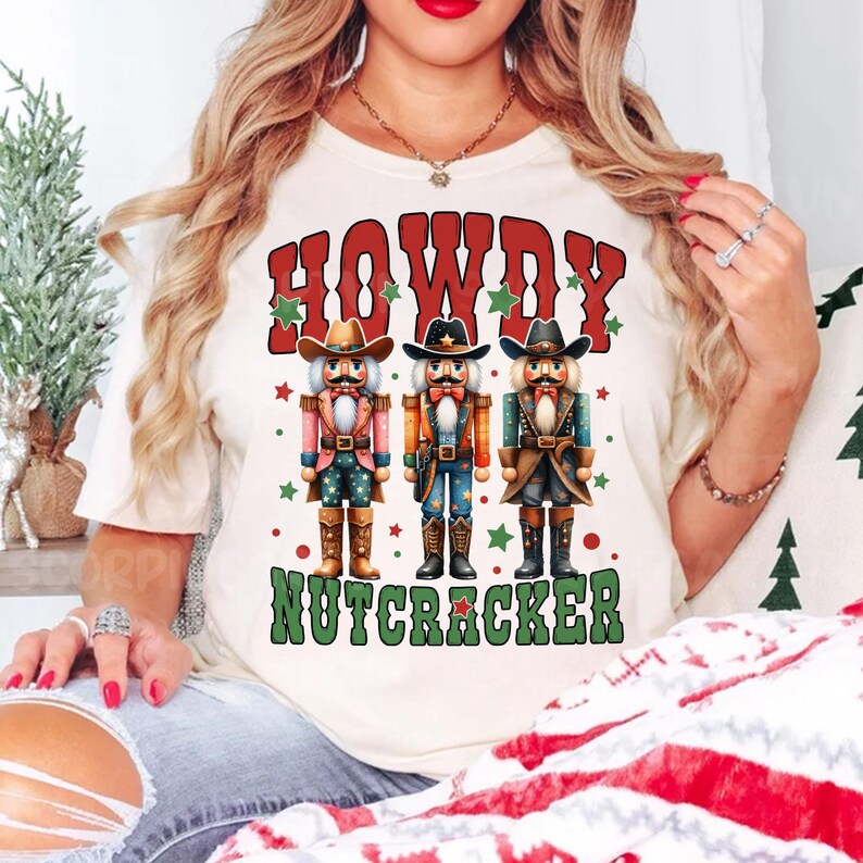Puede incluir: Camiseta blanca con un gr&aacute;fico de tres cascanueces vaqueros y el texto "Howdy Nutcracker".