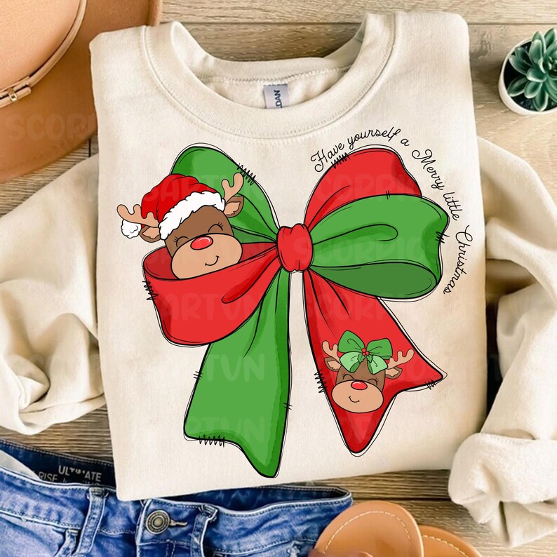 Pu&ograve; includere: Una felpa beige con un fiocco verde e rosso con una renna che spunta dal fiocco. Il testo "Have yourself a Merry little Christmas" &egrave; scritto sulla felpa.