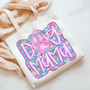 May include: A white tote bag with a pink and purple design that says "Dog Mama" with a pink paw print in the middle. The design is surrounded by colorful flowers.