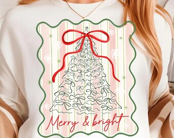 May include: White sweatshirt featuring a Christmas tree design with a red bow and the text "Merry & bright." The tree is outlined in white with green accents, set against a pink and white striped background.