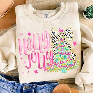 May include: A cream-colored sweatshirt with a pink "Holly Jolly" graphic and a green Christmas tree with a black and white polka dot bow.