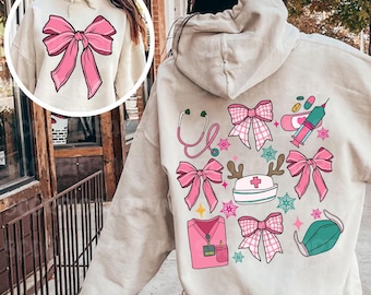 May include: A light grey hoodie with a pink bow on the front and a design on the back featuring pink bows, a stethoscope, a nurse's hat, a syringe, a bandage, and a face mask.