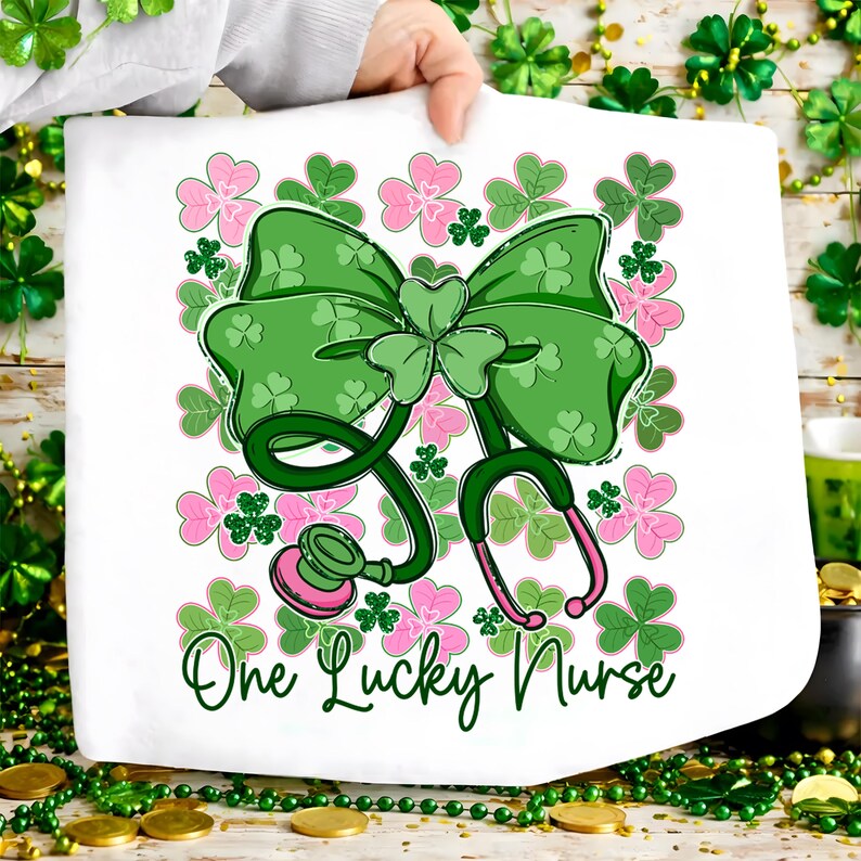 May include: White towel featuring a green bow with shamrock details and a stethoscope. Pink and green shamrocks surround the bow and stethoscope. The text "One Lucky Nurse" is written in green script below the stethoscope.