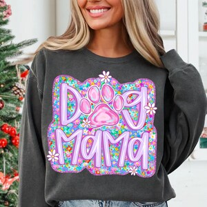 May include: A dark gray sweatshirt with a purple and pink graphic design that says "Dog Mama" surrounded by colorful flowers. The graphic also includes a pink paw print.