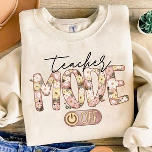 May include: A beige sweatshirt with a floral design that says "Teacher Mode Off" with a power button graphic.