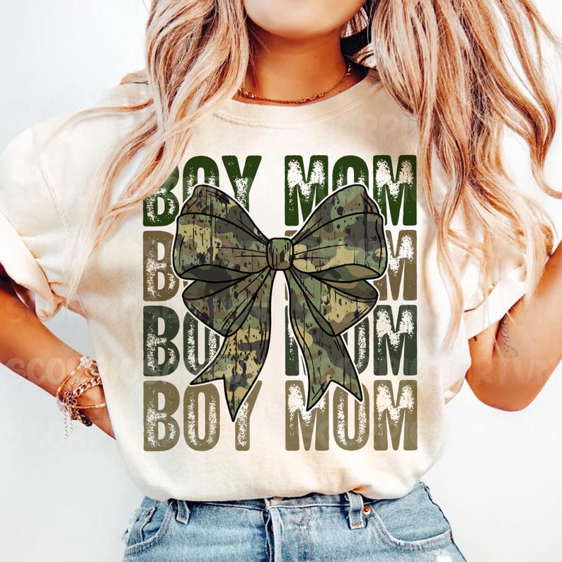 May include: A white t-shirt with the text "BOY MOM" repeated four times in a faded, distressed font. A large camouflage bow is centered on the shirt.