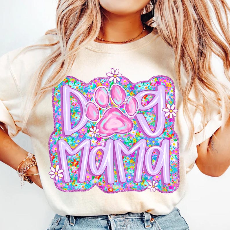 May include: A white t-shirt with a purple and pink graphic design that says "Dog Mama" with a pink paw print in the center. The graphic is surrounded by a floral pattern.