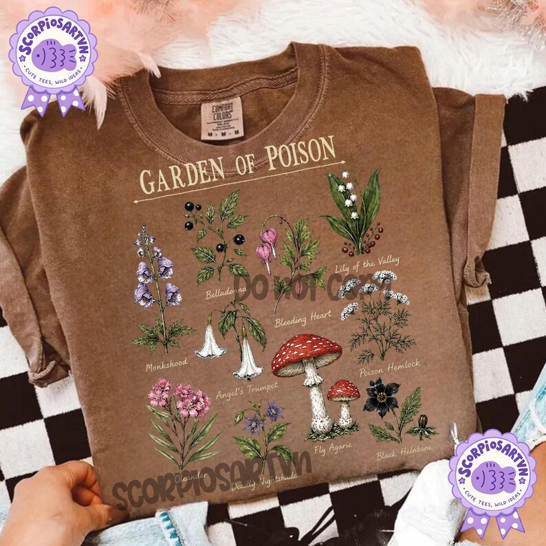 以下が含まれることがあります： Garden of Poisonというタイトルのグラフィックプリントが施された茶色の半袖Tシャツ。トリカブト、ベラドンナ、ケマンソウ、スズラン、エンゼルトランペット、ドクニンジン、ベニテングタケ、クリスマスローズなどの植物の植物画が描かれており、それぞれの名前が下に印刷されています。