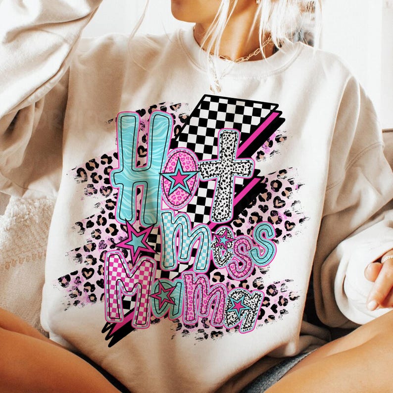 May include: White sweatshirt with a graphic design featuring the text "Hot Mess Mama" in pink, blue, and black lettering. The design also includes a checkered pattern, leopard print, and stars.