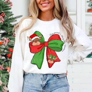 Pu&ograve; includere: Felpa bianca con un fiocco verde e rosso con un viso di renna che spunta dal fiocco. Il testo "Have yourself a Merry little Christmas" &egrave; scritto sulla felpa.