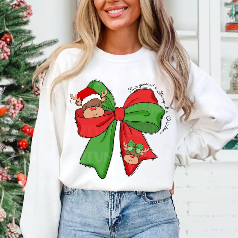 Pu&ograve; includere: Felpa bianca con un fiocco verde e rosso con un viso di renna che spunta dal fiocco. Il testo "Have yourself a Merry little Christmas" &egrave; scritto sulla felpa.