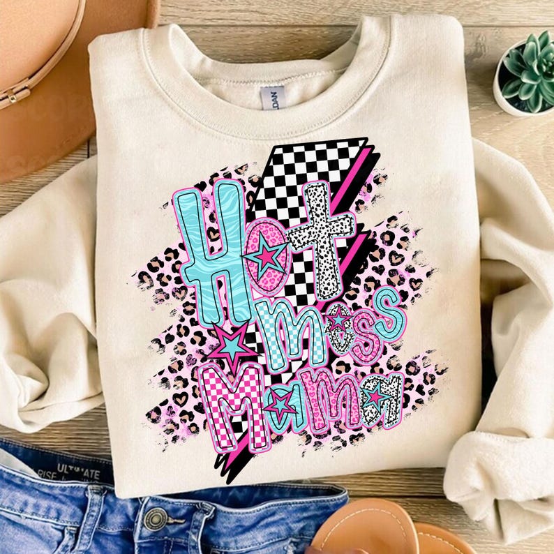 May include: A cream-colored sweatshirt with a graphic design that says "Hot Mess Mama" in pink, blue, and black lettering. The design features a checkered pattern, leopard print, and stars.