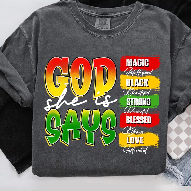 May include: A dark gray sweatshirt with the words "GOD she is SAYS" in a colorful design. The sweatshirt also features the words "MAGIC, Intelligent, BLACK, Beautiful, STRONG, Powerful, BLESSED, Brave, LOVE, Influential."