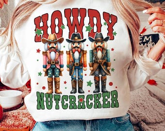 May include: White sweatshirt with a green, red, and white design featuring three cowboy nutcracker figures and the text "Howdy Nutcracker".