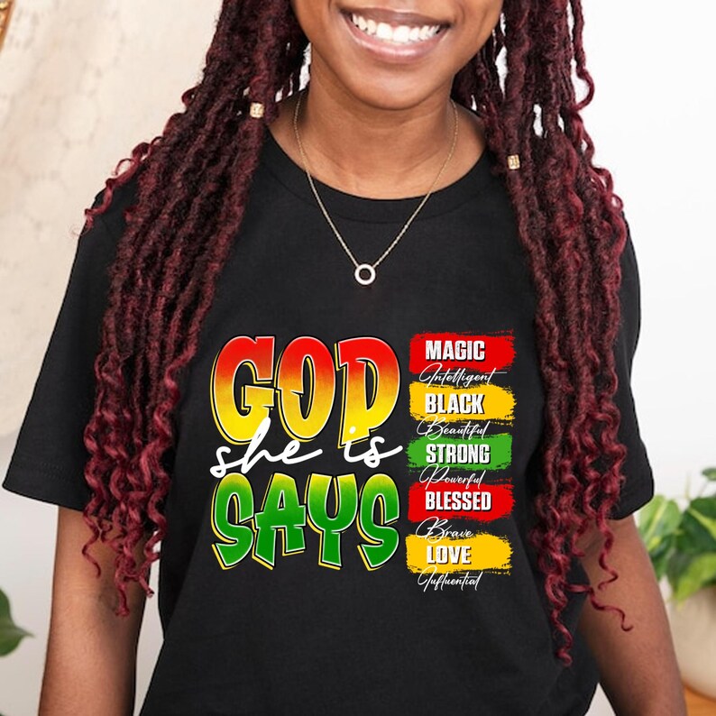 May include: Black t-shirt with the words "GOD she is SAYS" in yellow, green, and red. The shirt also features a list of words: Magic, Intelligent, Black, Beautiful, Strong, Powerful, Blessed, Brave, Love, and Influential.
