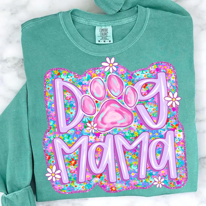 May include: A teal green t-shirt with a pink paw print and the text "Dog Mama" surrounded by colorful flowers.