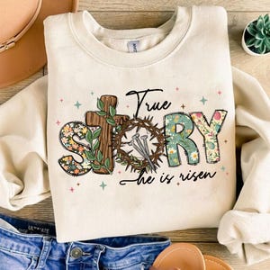 May include: A cream colored sweatshirt with a floral design that says "True Story" with a cross and a crown of thorns. The text below the design says "He is risen".