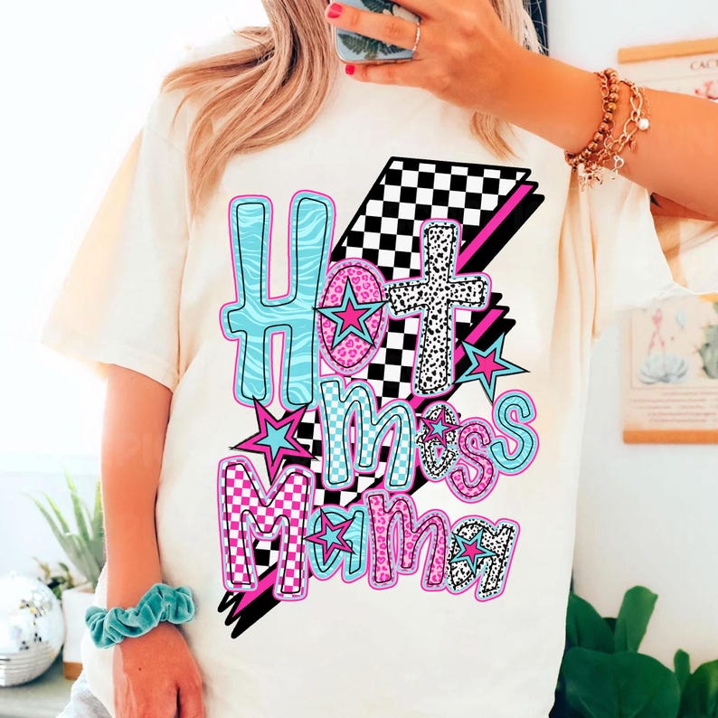 May include: White t-shirt with a graphic design that says "Hot Mess Mama" in pink, blue, and black letters with stars and checkered patterns.