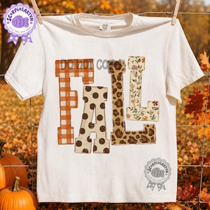 Pode incluir: Uma t-shirt de manga curta cor de creme com a palavra FALL em letras grandes. O F é xadrez laranja, o A é creme com bolinhas castanhas, o L tem padrão de leopardo castanho e o L tem um padrão floral creme.