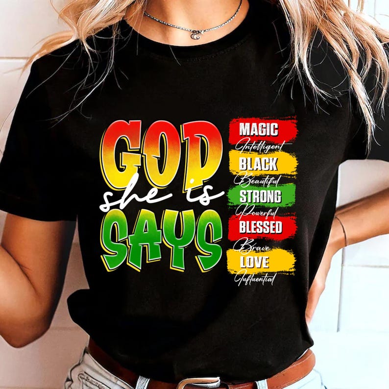 May include: Black t-shirt with the words "GOD she is SAYS" in yellow, red, and green. The shirt also features a list of words: MAGIC, Intelligent, BLACK, Beautiful, STRONG, Powerful, BLESSED, Brave, LOVE, and Influential.