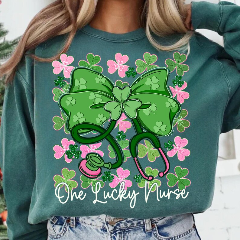 May include: Teal green sweatshirt with a St. Patrick's Day theme. The design features a large green bow with a shamrock, a stethoscope, and pink and green shamrocks. The text "One Lucky Nurse" is written in white script.