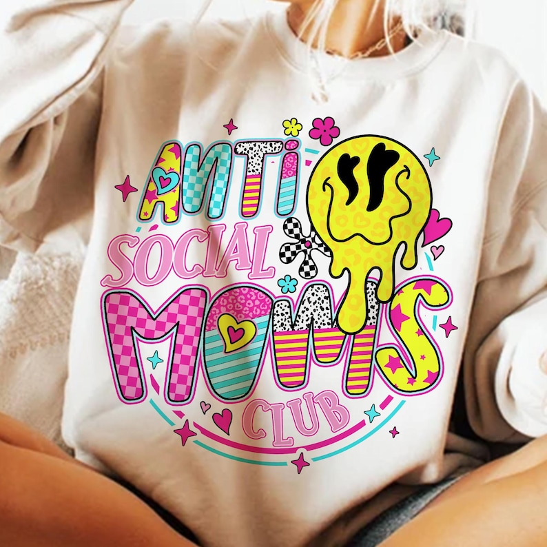 May include: Cream-colored sweatshirt with the text "ANTI SOCIAL MOMS CLUB" in a colorful, retro design. The design includes a melting yellow smiley face, hearts, stars, and checkered patterns. A fun, casual top.