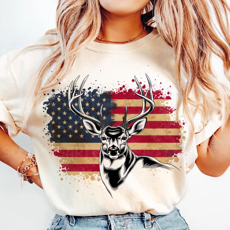 May include: A white t-shirt with a graphic of a deer with antlers in front of an American flag with a splatter paint effect.