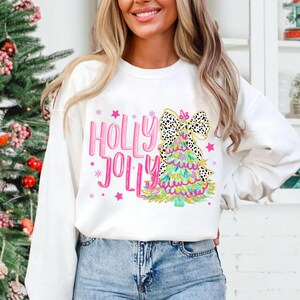 May include: White Christmas sweatshirt with a pink and green Christmas tree design and the text "Holly Jolly" in pink.