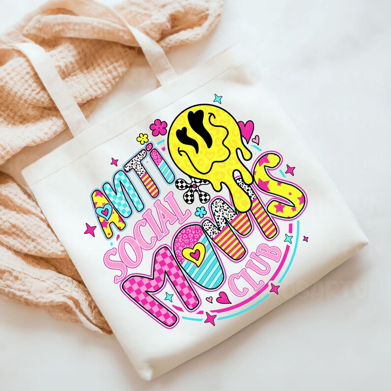 May include: White canvas tote bag with the words "ANTI SOCIAL MOMS CLUB" in a colorful, retro font. The design includes a yellow melting smiley face, hearts, stars, and floral accents. The bag has two white handles.